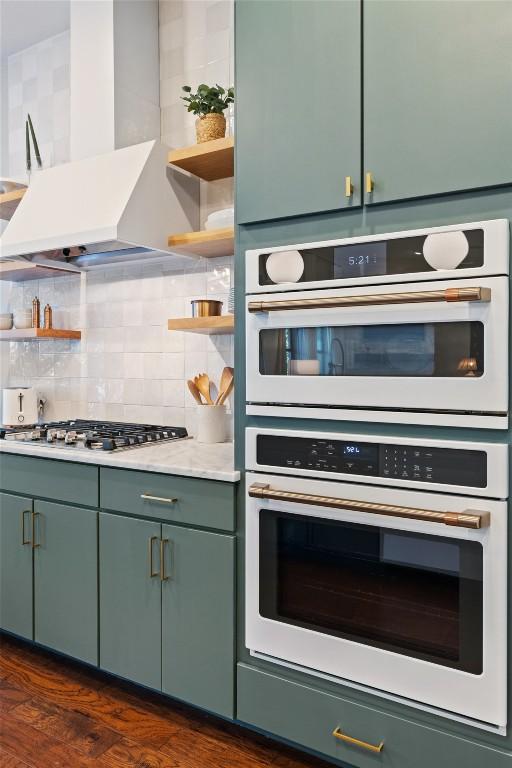 kitchen featuring double oven, stainless steel gas cooktop, dark hardwood / wood-style flooring, decorative backsplash, and wall chimney exhaust hood