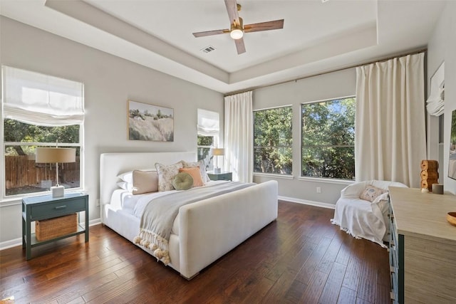 bedroom featuring dark hardwood / wood-style floors, a raised ceiling, and multiple windows