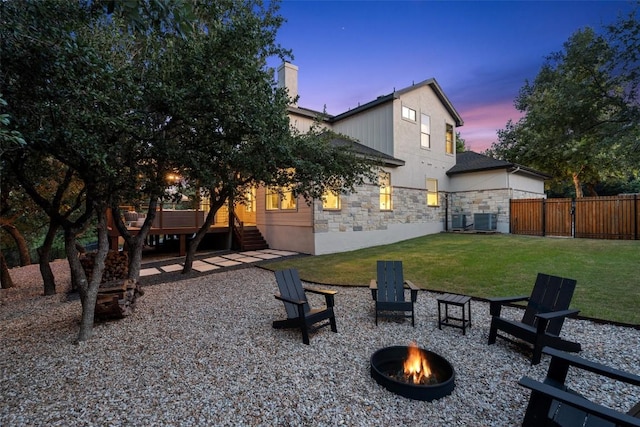 back house at dusk with cooling unit, a fire pit, and a lawn