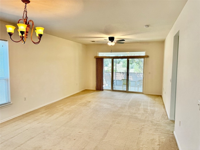 carpeted spare room featuring ceiling fan with notable chandelier