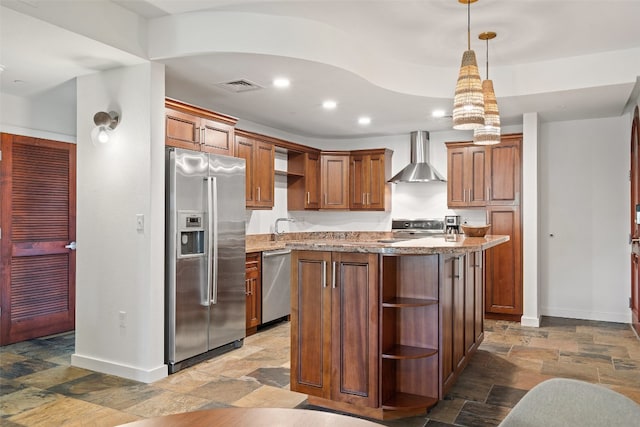 kitchen with pendant lighting, stainless steel appliances, a kitchen island, light stone countertops, and wall chimney range hood