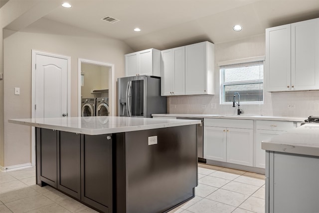 kitchen with washing machine and dryer, white cabinetry, a center island, and stainless steel refrigerator with ice dispenser