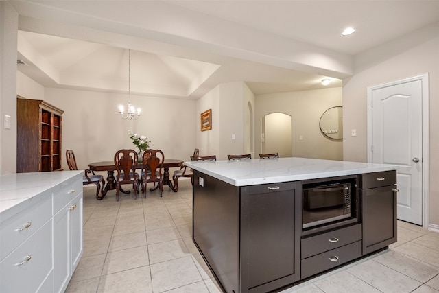 kitchen featuring a center island, light tile patterned floors, decorative light fixtures, light stone counters, and black microwave