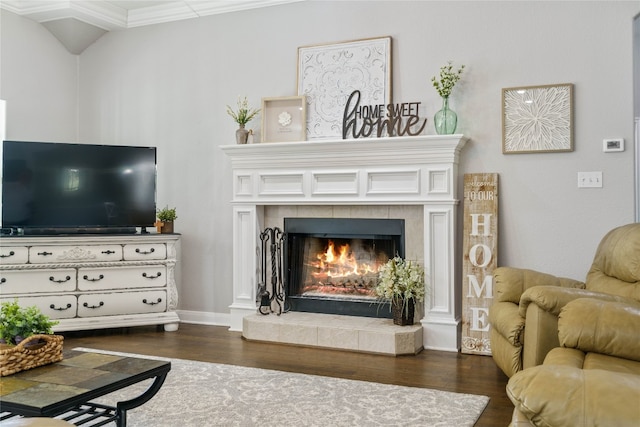 living room with crown molding, a tiled fireplace, and dark hardwood / wood-style floors