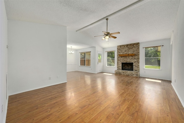 unfurnished living room with a healthy amount of sunlight, a brick fireplace, wood-type flooring, and ceiling fan with notable chandelier