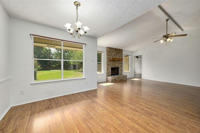 unfurnished living room featuring lofted ceiling, light wood-style flooring, a brick fireplace, a textured ceiling, and ceiling fan with notable chandelier