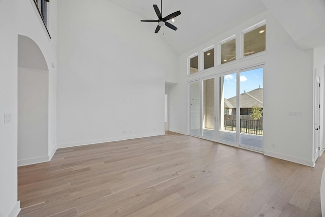 empty room with ceiling fan, light hardwood / wood-style floors, and a towering ceiling