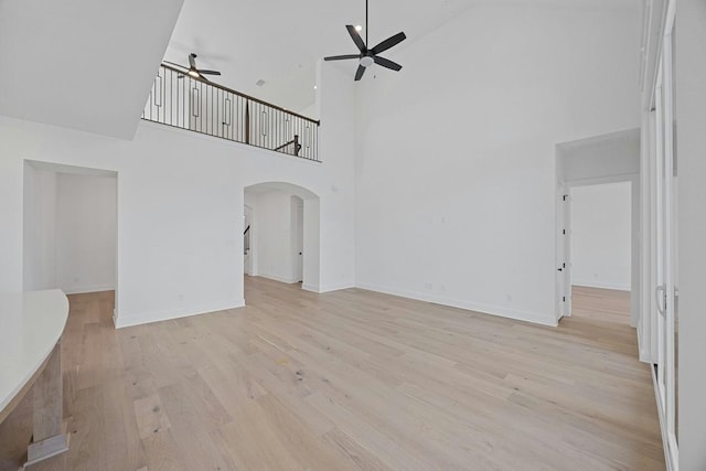 unfurnished living room with ceiling fan, a towering ceiling, and light hardwood / wood-style floors