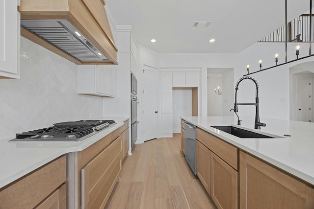 kitchen featuring appliances with stainless steel finishes, white cabinetry, sink, hanging light fixtures, and custom range hood