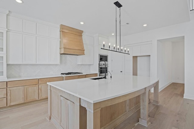 kitchen with white cabinetry, an island with sink, backsplash, custom range hood, and pendant lighting