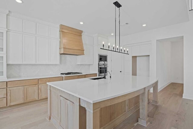 kitchen with white cabinetry, hanging light fixtures, light hardwood / wood-style flooring, appliances with stainless steel finishes, and an island with sink