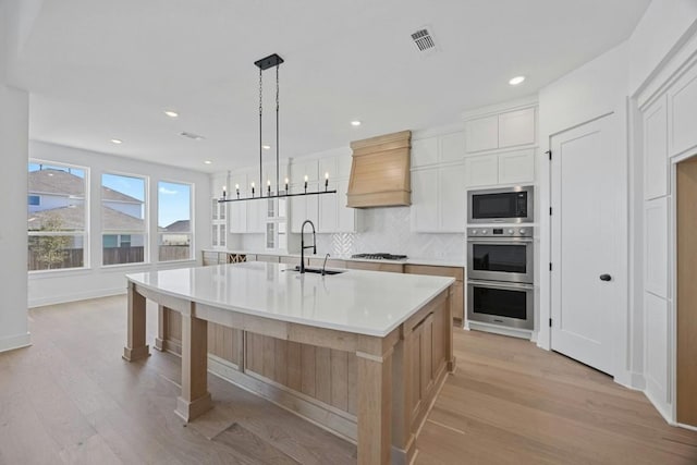 kitchen featuring sink, a large island with sink, pendant lighting, stainless steel appliances, and white cabinets