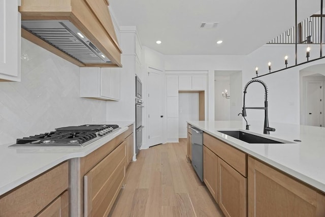 kitchen featuring sink, premium range hood, white cabinetry, stainless steel appliances, and decorative light fixtures