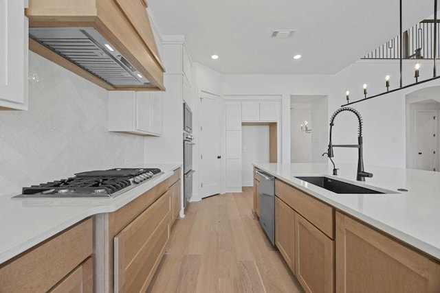 kitchen with premium range hood, appliances with stainless steel finishes, decorative light fixtures, sink, and white cabinets