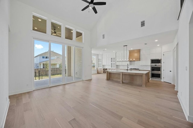 unfurnished living room featuring sink, a towering ceiling, ceiling fan, and light wood-type flooring