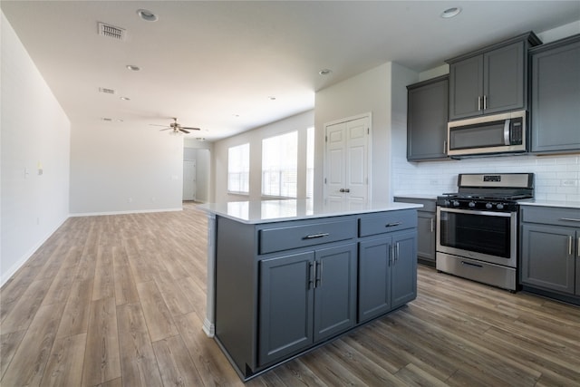 kitchen with appliances with stainless steel finishes, decorative backsplash, a kitchen island, and hardwood / wood-style floors