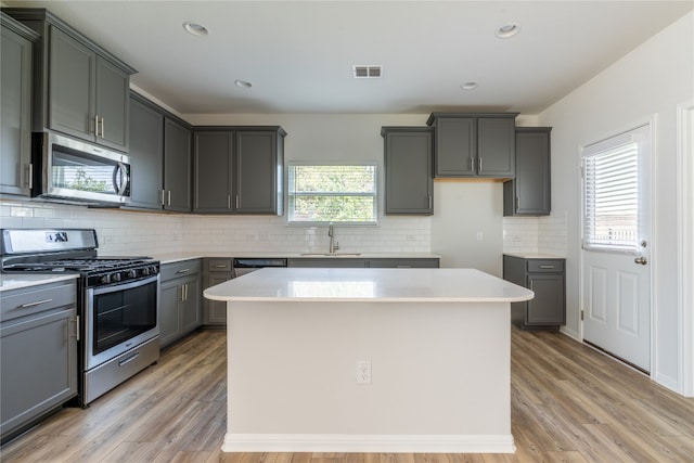 kitchen featuring gray cabinets, a center island, backsplash, light wood-type flooring, and stainless steel appliances