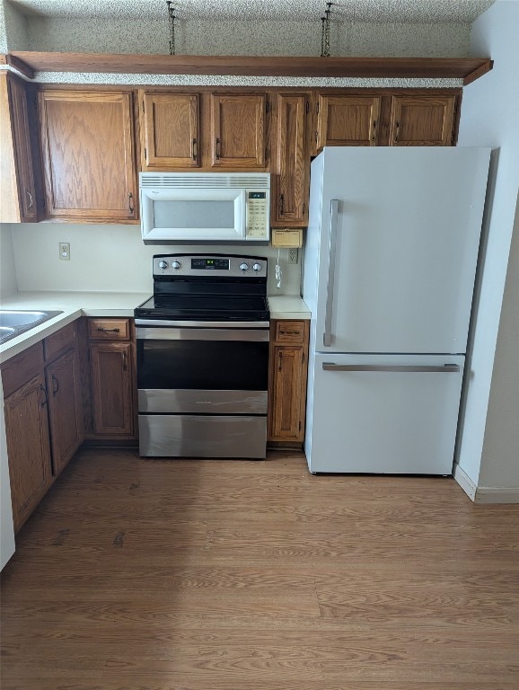 kitchen with sink, a textured ceiling, white appliances, and hardwood / wood-style floors