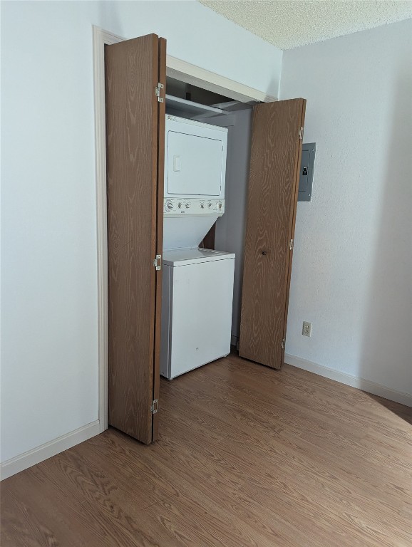 laundry area with electric panel, hardwood / wood-style flooring, a textured ceiling, and stacked washer / drying machine