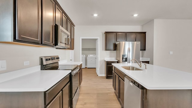 kitchen featuring stainless steel appliances, a center island with sink, sink, light hardwood / wood-style flooring, and separate washer and dryer