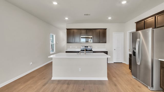 kitchen with light wood-type flooring, stainless steel appliances, dark brown cabinets, and a center island with sink