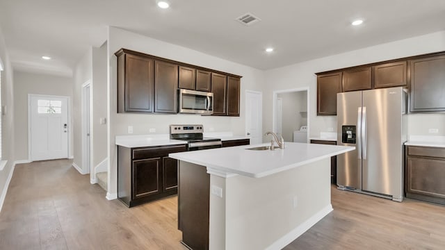 kitchen with appliances with stainless steel finishes, light wood-type flooring, and a center island with sink