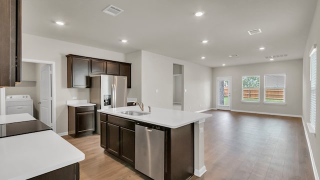 kitchen featuring appliances with stainless steel finishes, an island with sink, sink, washer / dryer, and light hardwood / wood-style flooring