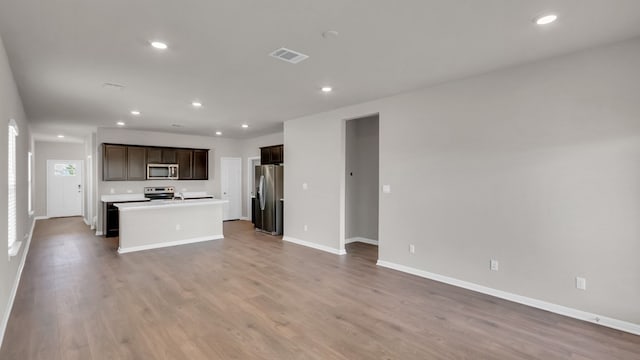 kitchen with appliances with stainless steel finishes, a kitchen island with sink, hardwood / wood-style floors, and dark brown cabinetry