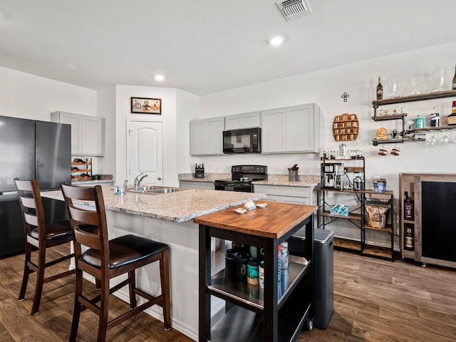 kitchen featuring a center island with sink, gray cabinets, visible vents, a sink, and black appliances