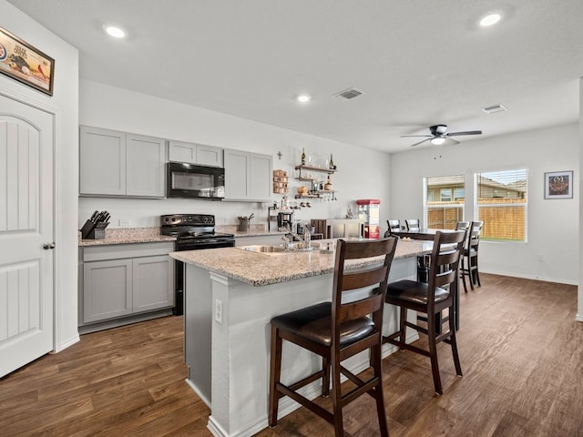 kitchen with sink, black appliances, dark wood-type flooring, ceiling fan, and a breakfast bar