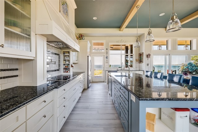 kitchen featuring pendant lighting, backsplash, dark stone counters, beam ceiling, and light hardwood / wood-style floors