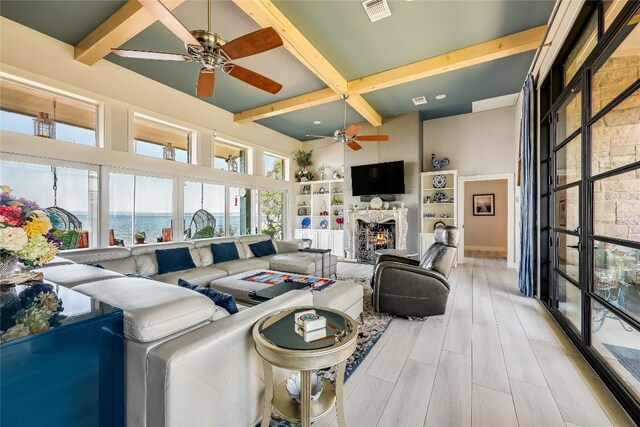 living room with beamed ceiling, ceiling fan, a high ceiling, and light hardwood / wood-style floors