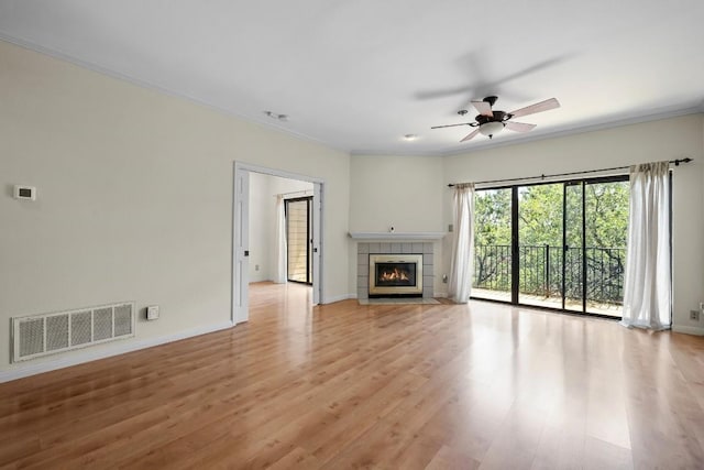 unfurnished living room with crown molding, ceiling fan, a tiled fireplace, and light hardwood / wood-style flooring