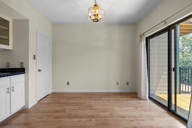 unfurnished dining area featuring ornamental molding, light wood-type flooring, and an inviting chandelier