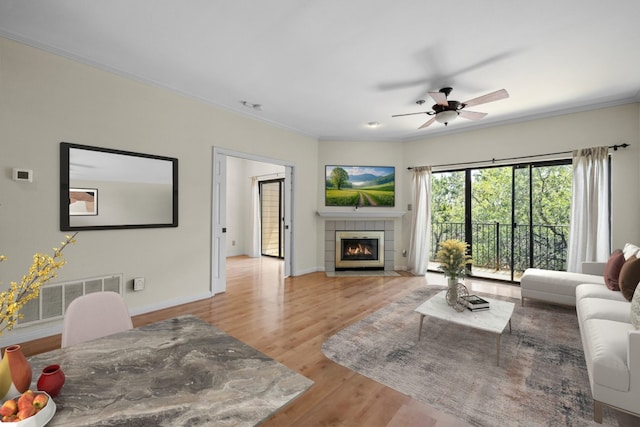 living room featuring ceiling fan, ornamental molding, light hardwood / wood-style floors, and a tile fireplace