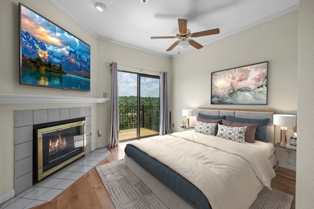 bedroom with crown molding, ceiling fan, light hardwood / wood-style floors, a tiled fireplace, and access to outside