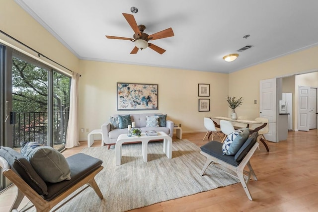 living area with ceiling fan, visible vents, baseboards, ornamental molding, and light wood finished floors