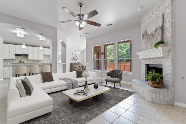 tiled living room with ceiling fan and a brick fireplace