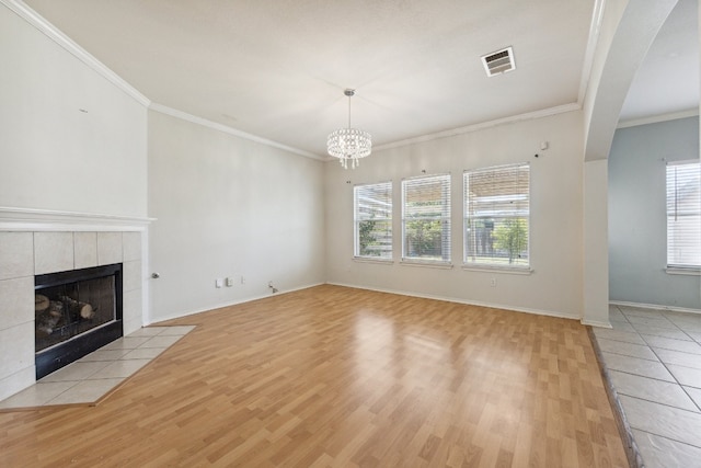 unfurnished living room with a tiled fireplace, ornamental molding, an inviting chandelier, and light hardwood / wood-style floors