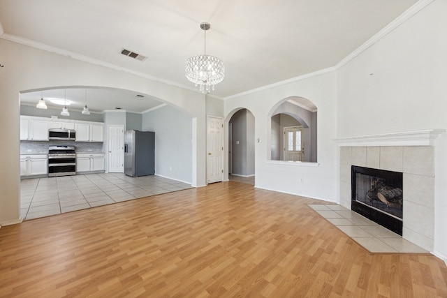 unfurnished living room featuring a tiled fireplace, light hardwood / wood-style flooring, a notable chandelier, and ornamental molding