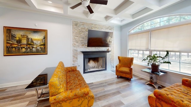 living room with beam ceiling, light wood-type flooring, a stone fireplace, and coffered ceiling