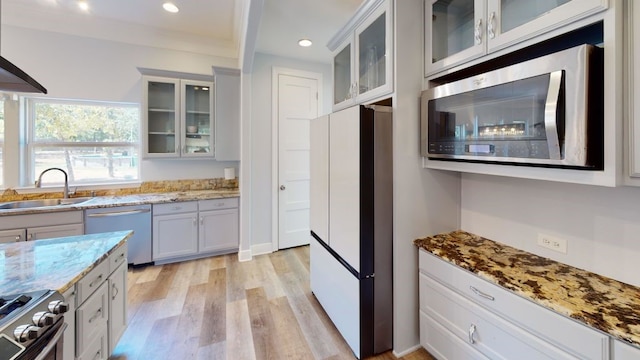 kitchen with sink, appliances with stainless steel finishes, light hardwood / wood-style floors, light stone counters, and white cabinetry