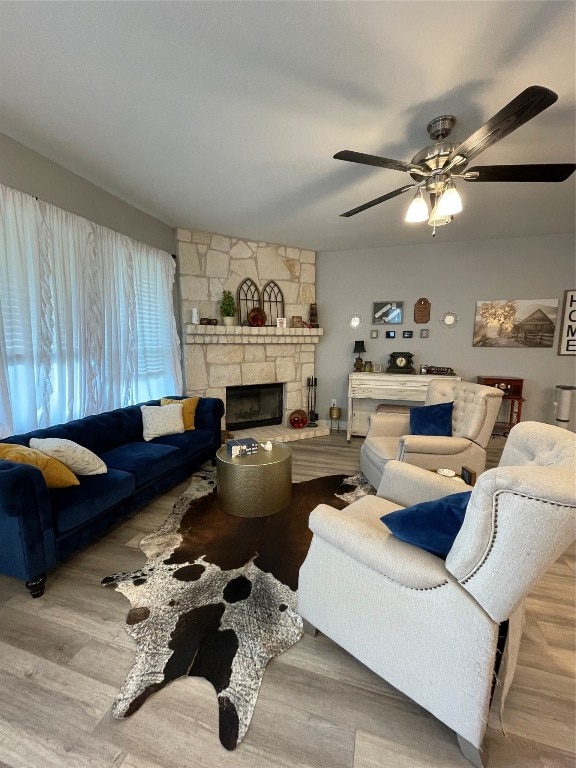 living room with light hardwood / wood-style floors, a stone fireplace, and ceiling fan