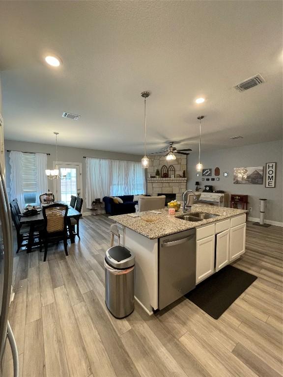 kitchen featuring sink, a stone fireplace, light hardwood / wood-style flooring, stainless steel dishwasher, and white cabinetry