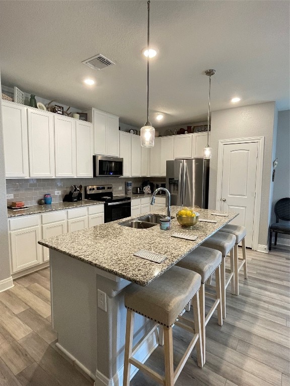 kitchen featuring light wood-type flooring, hanging light fixtures, sink, a center island with sink, and stainless steel appliances