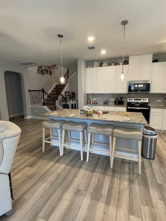 kitchen featuring stainless steel appliances, light stone counters, light wood-type flooring, white cabinets, and hanging light fixtures