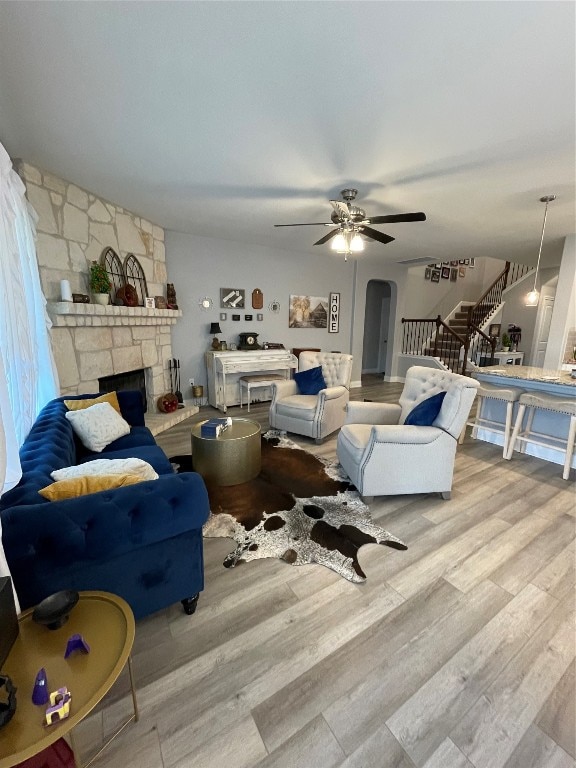 living room with ceiling fan, light hardwood / wood-style flooring, and a stone fireplace