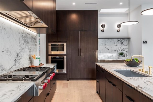 kitchen featuring backsplash, sink, range hood, appliances with stainless steel finishes, and decorative light fixtures