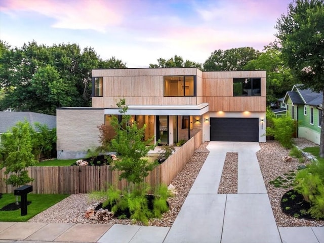 modern home featuring a garage, covered porch, driveway, and fence