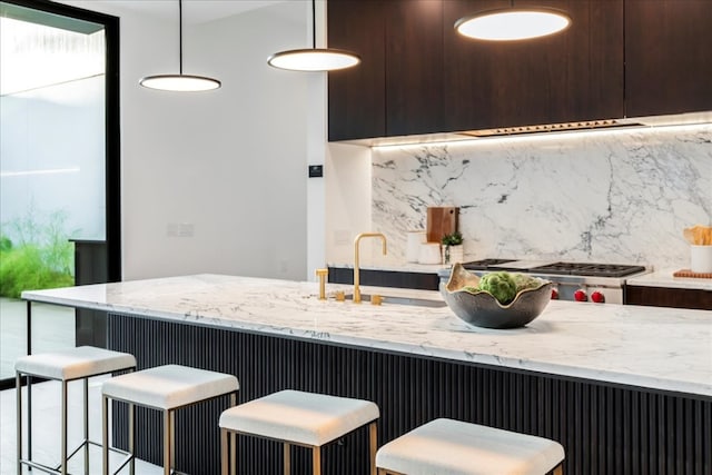 kitchen with pendant lighting, a breakfast bar, backsplash, sink, and light stone counters